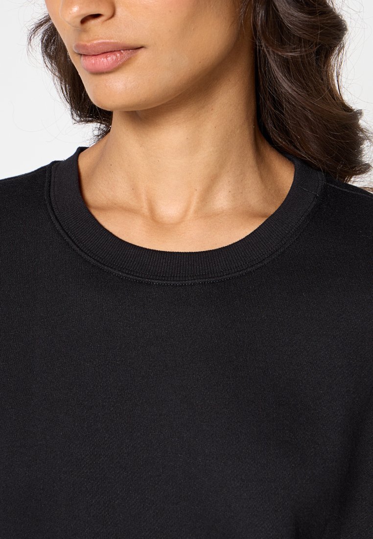 Sweatshirt noir avec un col rond à côtes et une texture douce. Vue en gros plan mettant en avant la douceur du tissu et le design épuré.