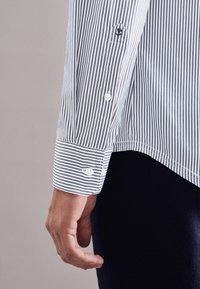 Gestreiften Hemd mit blauen und weißen vertikalen Streifen, mit weißen Knopfmanschetten und einem kleinen Logo auf der Brusttasche.