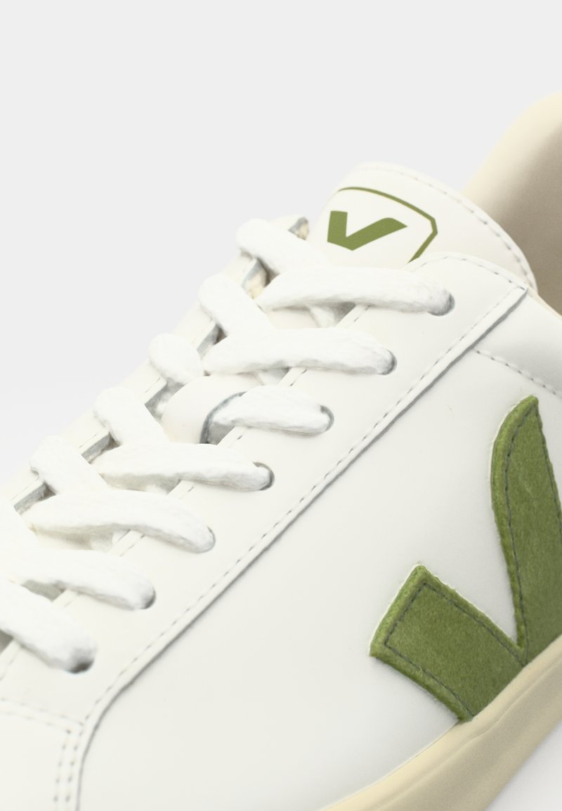 Basket en cuir végétalien blanc avec des accents en daim vert, bout rond et lacets plats blancs. Présente un logo vert sur la languette.