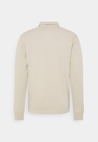 Polo à manches longues en coton beige doux, doté d'un col classique et de poignets côtelés. Design simple sans motifs ni graphismes.