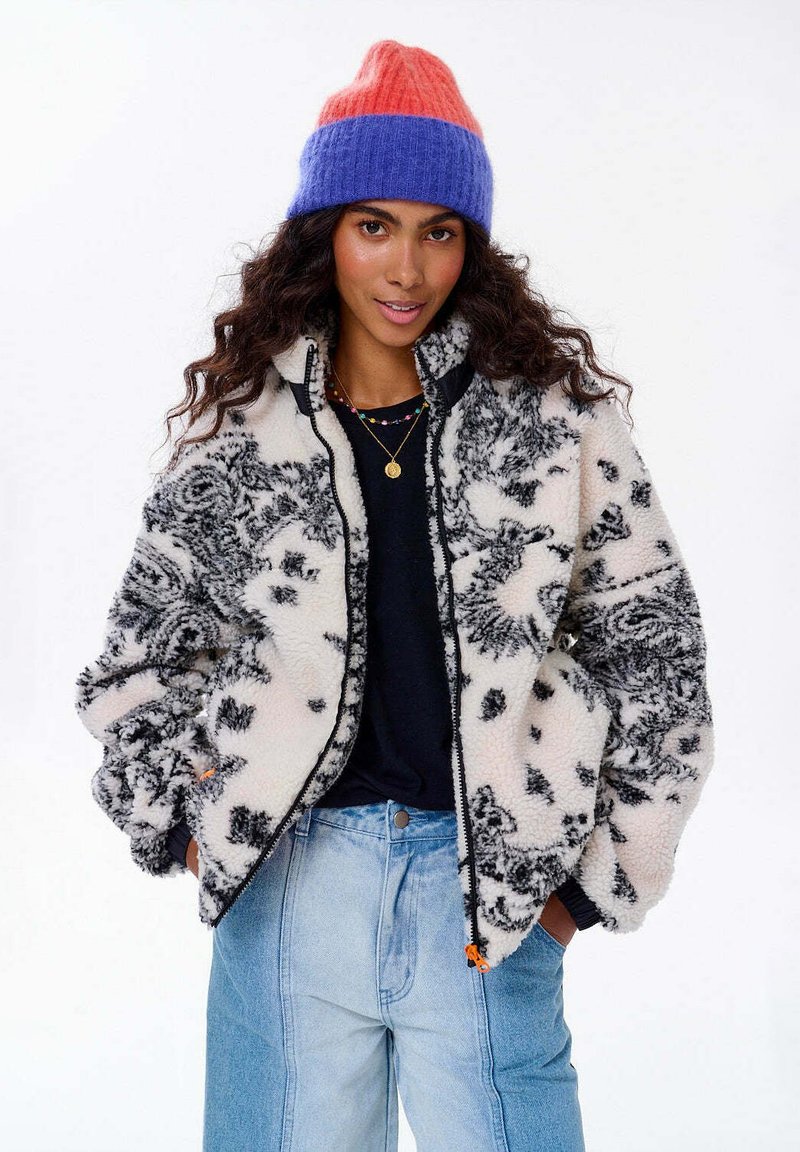 Fleece bunda v krémovej farbe s čiernym kvetinovým vzorom, so zipsom a bočnými vreckami; spárovaná s multikolórovou pletenou čiapkou.