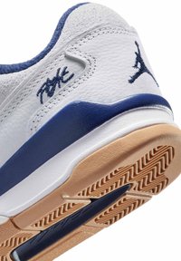 Vit och blå sneakerhäl med texturerad ljusbrun sula, prydd med broderad mörkblå Jumpman-logotyp och signaturdetalj.