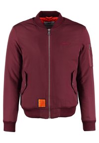 Mörkröd bomberjacka med ribbad krage och manschetter. Har frontdragkedja, sidofickor och en ficka på ärmen med dragkedja, med en orange etikettdetalj.
