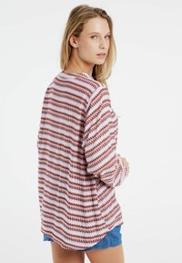 Camicia a maniche lunghe, dal taglio morbido, con un motivo a righe nei colori rosso, rosa e bianco. Il tessuto sembra lavorato a maglia e presenta una texture con un orlo curvo.