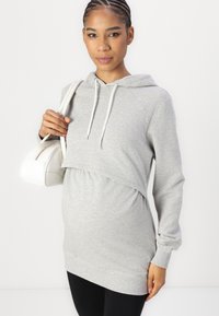 Sweatshirt de maternidade cinza claro com bolso canguru, capuz com cordão e barra franzida. Combinado com leggings pretas e uma pequena bolsa branca.