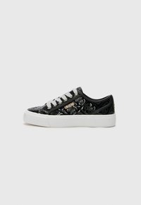 Svarta sneakers med en glänsande, texturerad yta med ett blommönster, vit sula och grå snörning. Gyllene "GUESS"-logotyp på sidan.