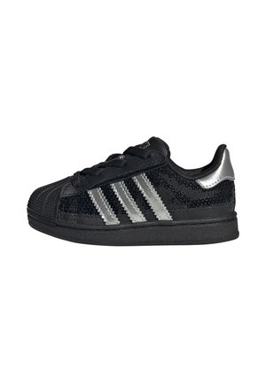 Zwarte Adidas-sneaker met zilveren strepen, zwarte zool, veters en een zilveren hielstuk, versierd met zwarte pailletten.
