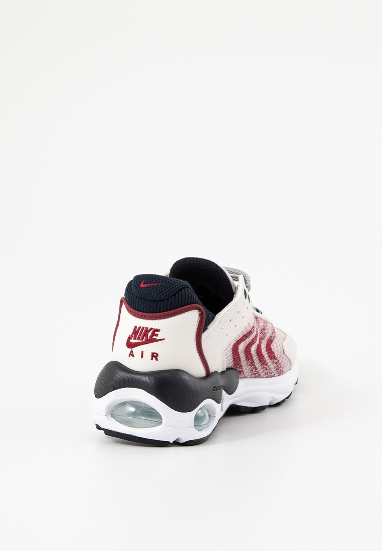 Sneaker Nike Air con tomaia in mesh rosso e bianco, dettagli blu e un'unità air visibile nella suola nera. Finitura testurizzata sul tallone.