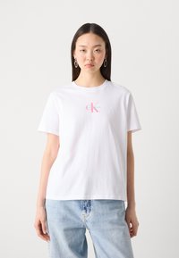 Balta medvilninė marškinė su trumpomis rankovėmis, su rožine ir mėlyna Calvin Klein logotipu ant krūtinės. Atpalaiduotas siluetas.