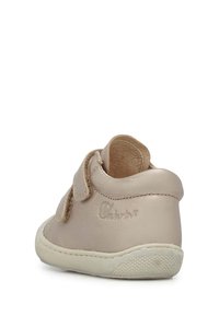 Zapato para niño pequeño de cuero beige con una textura suave, que presenta dos correas de Velcro, punta redondeada y una suela de goma con un agarre estampado.