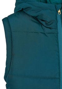 Gilet matelassé teal avec une capuche et une fermeture éclair visible. Le tissu a une texture lisse avec des coutures décoratives.