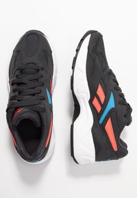 Czarne buty sportowe z siateczkową i zamszową cholewą, z niebieskimi i czerwonymi akcentami, amortyzowaną podeszwą oraz zaokrąglonym przodem.