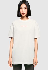 Weißes, übergroßes Baumwoll-T-Shirt mit kurzen Ärmeln, das auf der Brust "DOUCEUR FLORALE" in Rot aufgedruckt hat, mit glatter Textur.