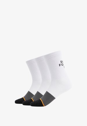 Trois paires de chaussettes de crew, présentant une texture côtelée. Blanches avec des accents noirs, gris et orange. Le texte sur le côté indique "NE PAS SUIVRE."