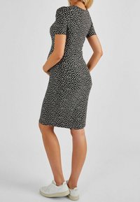 Svart figursydd klänning prydd med små vita blommönster, korta ärmar och rund halsringning, i kombination med vita sneakers.