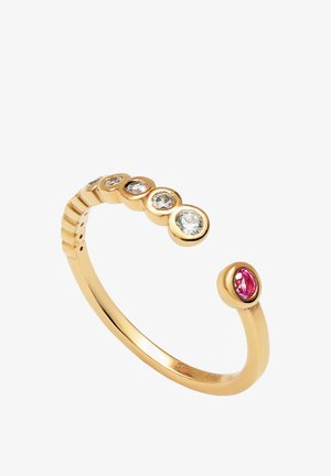 Złoty pierścionek o zakrzywionym kształcie, z sześcioma okrągłymi oprawami z przezroczystymi kamieniami oraz jednym różowym kamieniem na końcu. Gładka, polerowana powierzchnia.