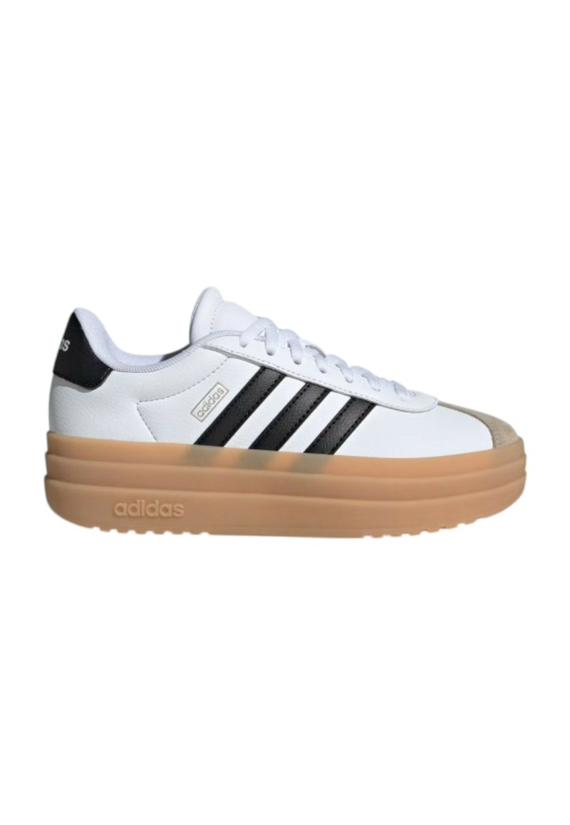 Zapatilla deportiva blanca con un talón negro texturizado, tres rayas negras y una suela de plataforma marrón. Presenta materiales de cuero liso y tela.