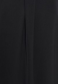 Tissu noir avec une couture verticale centrale montrant une texture subtile et une légère ombre sur un fond textile uni.