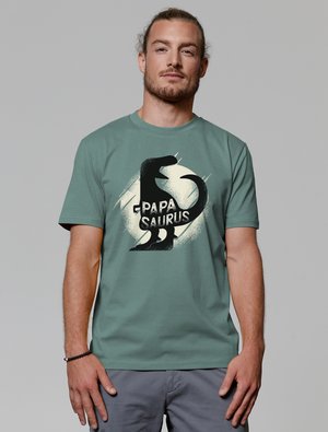 Groene katoenen T-shirt met een grafisch ontwerp van een zwarte beer en de tekst "Papa Saurus" in verweerde lettertype. Korte mouwen, ronde hals.