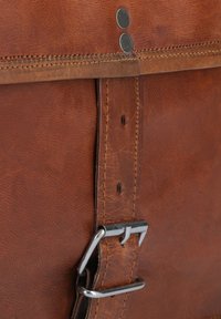 Close-up van een bruine leren tasriem met metalen gesp en gestikte randen.