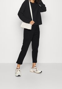 Czarny krótki sweatshirt, dopasowane czarne spodnie i kremowa torebka na ramię. Białe buty sportowe z brązowymi akcentami. Gładkie tekstury materiałów.