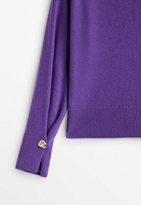 Pull violet à manches longues avec ourlet et poignets côtelés, avec un petit charm en forme de cœur doré sur la fente du poignet.