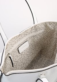 Witte lederen schoudertas met zwarte accenten, met een interieur van stof met bloemenpatroon en een klein ritsvakje.