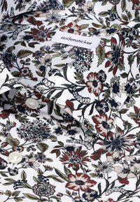 Bloemenoverhemd met een witte achtergrond en rode, marineblauwe en groene patronen. Voorzien van een label dat in de kraag is genaaid en een knoopsluiting.