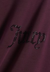 Σκούρο μωβ ύφασμα με τη λέξη "Tilly" γραμμένη με μικρές μαύρες και λευκές στρας σε καλλιγραφική γραφή.