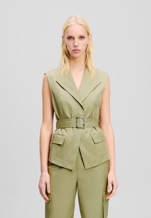 Khaki mouwloze blazer met een wikkelontwerp, een brede riem met een vierkante gesp en twee voorkwabben. Gladde stof met een subtiele glans.