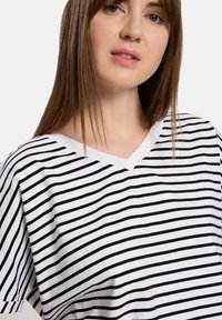 T-shirt w paski w białym i czarnym kolorze. Posiada krótki rękaw, luźny krój i miękką teksturę materiału.