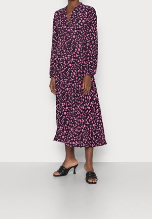 Robe à manches longues noire avec un motif de feuilles roses, col boutonné et bas évasé. Associée à des sandales à talons noires.
