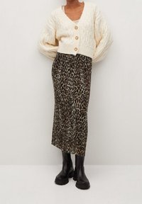 Objemný krémový kardigan s pletením do kabelů a dřevěnými knoflíky, ve spojení se přiléhavou midi sukní s leopardím potiskem a černými robustními botami.