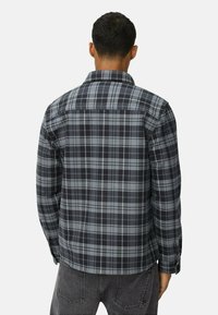 Chemise en plaid gris �à manches longues, col boutonné et empiècement au dos. Présente des carreaux gris foncé et clair, avec une texture lisse.