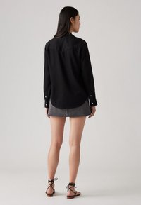 Svart langermet skjorte med buet nederkant, kombinert med et grått denim miniskjørt og svarte snøring sandaler. Jevn tekstur, avslappet passform.