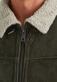 Dunkelgrüne Wildlederjacke mit einem strukturierten, cremeweißen Schafwollkragen, ausgestattet mit einem Metallreißverschluss und dekorativen Hardware-Details.