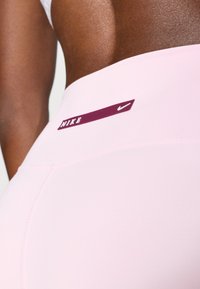 Rózsaszín, magas derekú leggings sima textúrával, a derékrészen bordó Nike logóval és letisztult varrási részletekkel.