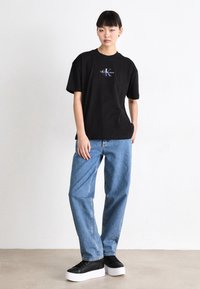 Czarny bawełniany t-shirt z krótkim rękawem z kolorowym logo "Calvin Klein Jeans", w połączeniu z jasnoniebieskimi dżinsami i czarnymi sneakersami na platformie.