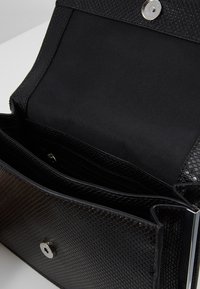 Borsa a clutch in pelle nera con texture aperta, che mostra un interno foderato in tessuto con scomparti con zip e aperti, e chiusura a scatto magnetico in argento.
