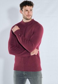 Bordeauxroter, gerippter Pullover mit hohem Kragen, langen Ärmeln und taillierter Silhouette. Verfügt über dezente Steppnähte und strukturierte Stoffoberfläche.