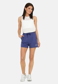 Lilla sportsshorts med elastisk talje og snøre, parret med en hvid ærmeløs top. Har sidelommer og logo detaljer.