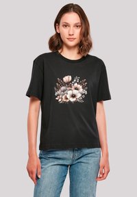 Black short-sleeve t-shirt featuring a floral graphic print in soft colors, with a round neckline and relaxed fit. Worn with light blue jeans.