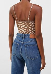 Top con righe zebra marroni e crema, rifinito con pizzo, abbinato a jeans in denim blu a vita alta con etichetta in pelle sul retro.