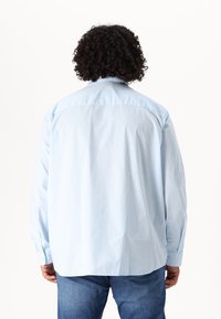 Camicia azzurro chiaro a maniche lunghe con bottoni, realizzata in cotone. Presenta un colletto classico, dettaglio sulla parte superiore delle spalle e polsini regolabili. Vestibilità casual.