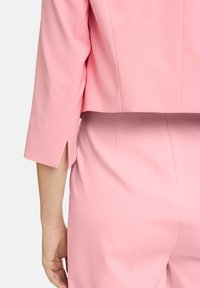 Różowa krótka marynarka z rękawami o długości trzech czwartych, charakteryzująca się prostym wzornictwem i bocznymi rozcięciami. Gładka faktura materiału z dopasowanym krojem.