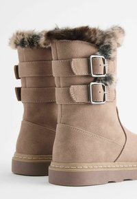 Botas de ante sintético de color marrón claro con un suave puño de piel de pelo, que presentan dos hebillas plateadas a un lado y una suela de goma.