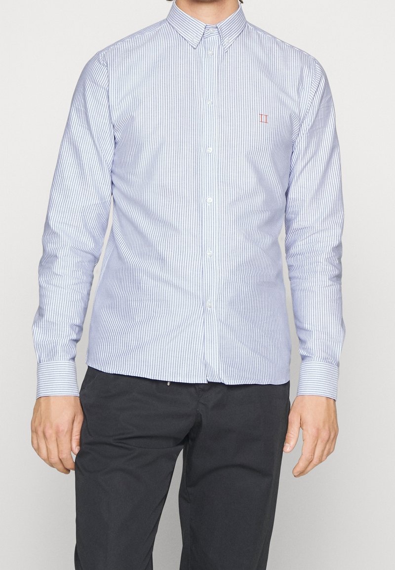 Camicia button-up a righe azzurre e bianche con colletto, dotata di maniche lunghe e un piccolo logo rosso sul petto. Tessuto dalla texture liscia.