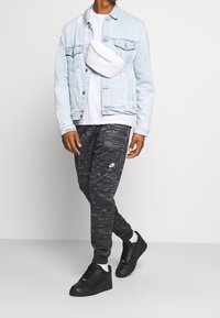 Neformální outfit zahrnující světle modrou džínovou bundu, bílou ledvinku, bílé tričko, černé vzorované tepláky a černé tenisky.