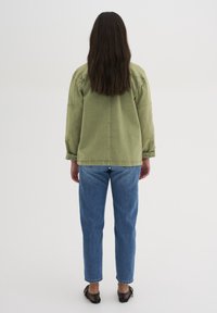 Oliwkowa, oversize kurtka z opadającymi ramionami, w zestawie z jasnoniebieskimi spodniami typu straight-leg. Obuwie z czarnym siateczkowym detalem.