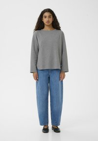 Maglietta grigia a maniche lunghe con vestibilità comoda, abbinata a jeans blu a vita alta e scarpe basse nere. Design semplice senza motivi visibili.